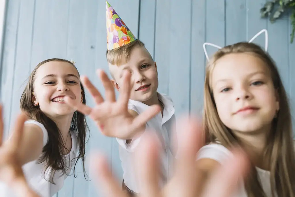 Drei fröhliche Kinder auf einem Kindergeburtstag lachen in die Kamera und strecken die Hände entgegen