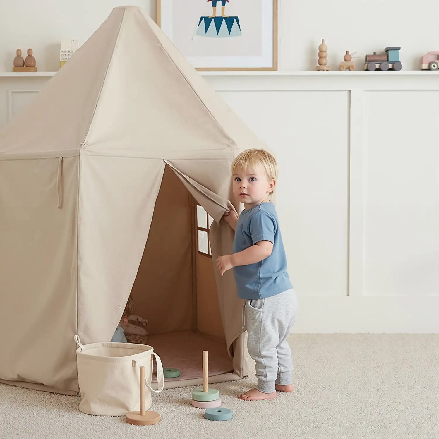 Kleinkind steht vor einem beigefarbenen Spielzelt im Kinderzimmer und schaut neugierig hinein