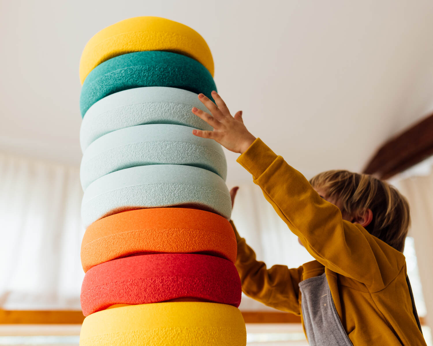 Kind stapelt bunte Stapelsteine im Innenraum; Bewegungsspielzeug, Stapelstein mieten bei LittleLoopa, kindgerechte F&ouml;rderung der Motorik.