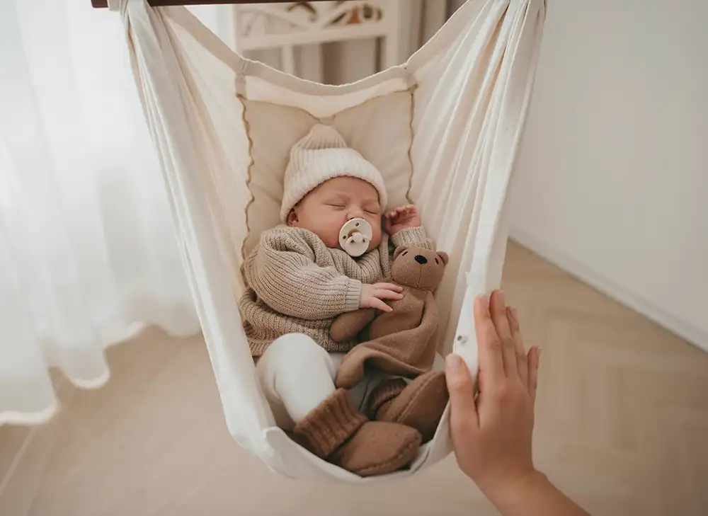 Friedlich schlafendes Baby in einer Federwiege, die die natürliche Körperhaltung und Geborgenheit unterstützt.